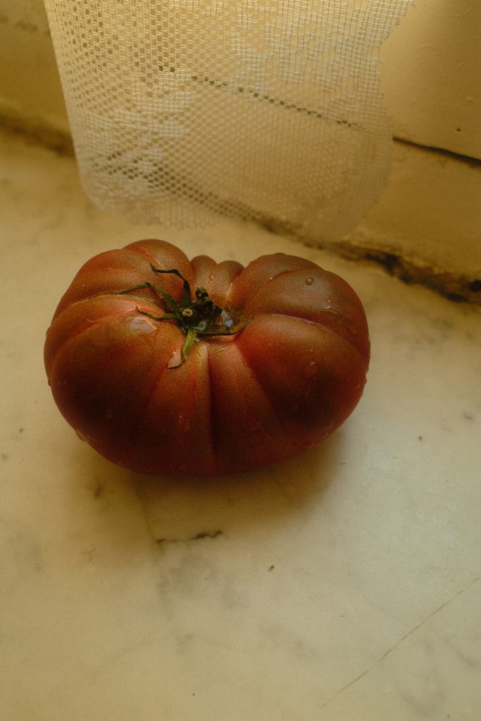 Rustic heirloom tomato resting on a marble surface with lace curtain in the background.