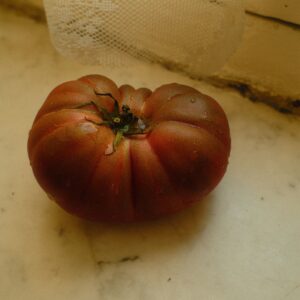 Rustic heirloom tomato resting on a marble surface with lace curtain in the background.